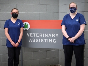 Two women standing in front of the Veterinary Assisting Sign